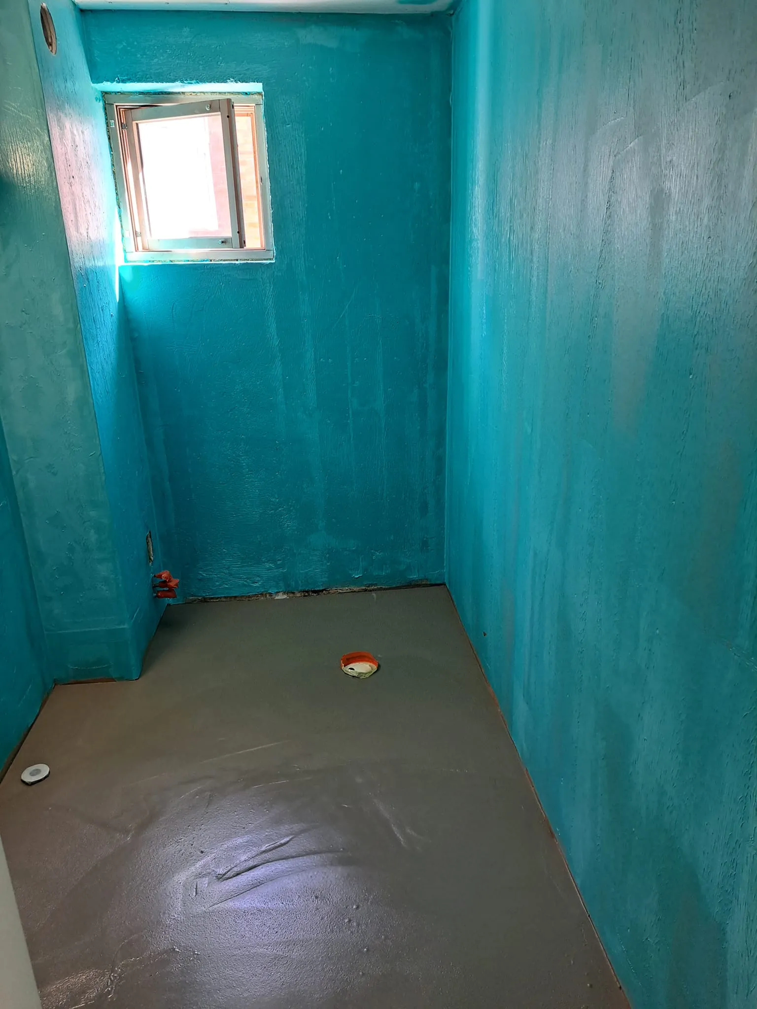 Turkoosi huone, harmaa lattia, ikkuna.