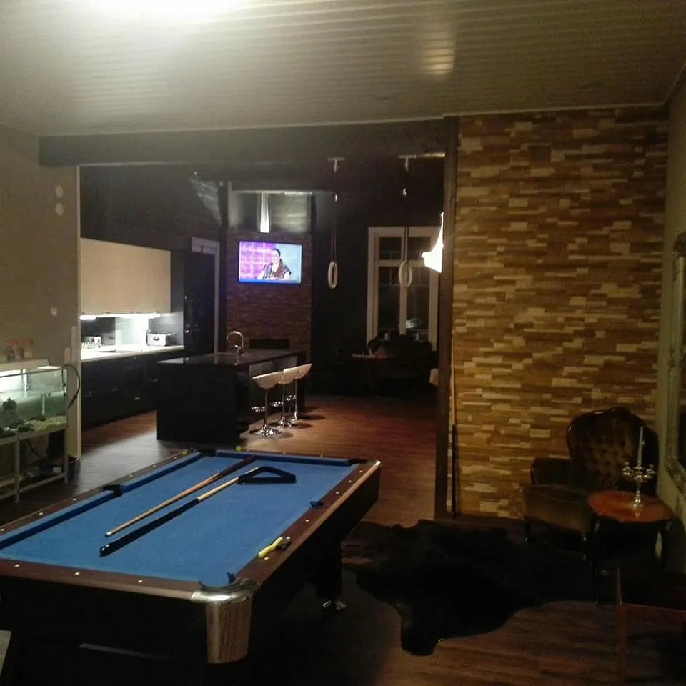 Sisätila, jossa on biljardipöytä, keittiö, baarituolit ja oleskelualue, jossa on tiiliseinä ja pehmeä valaistus.