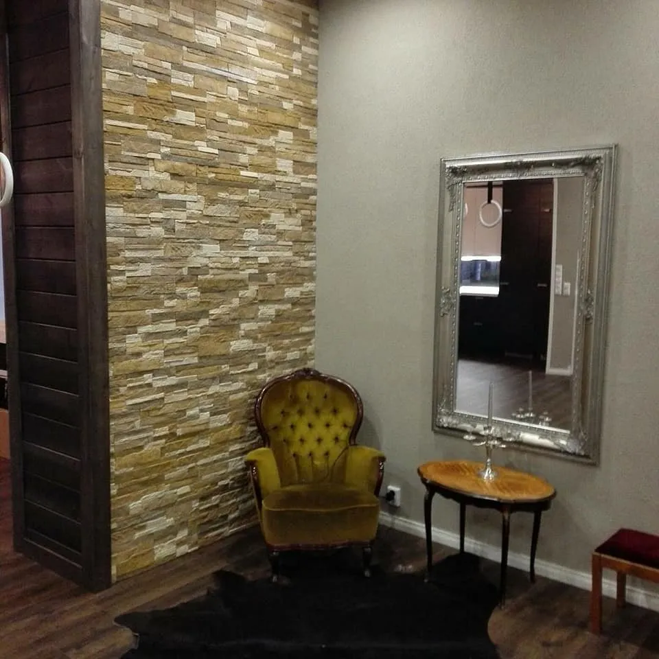 Olohuoneessa on kultainen nojatuoli, peili, pieni pöytä ja kiviseinä, valaistus on pehmeää.