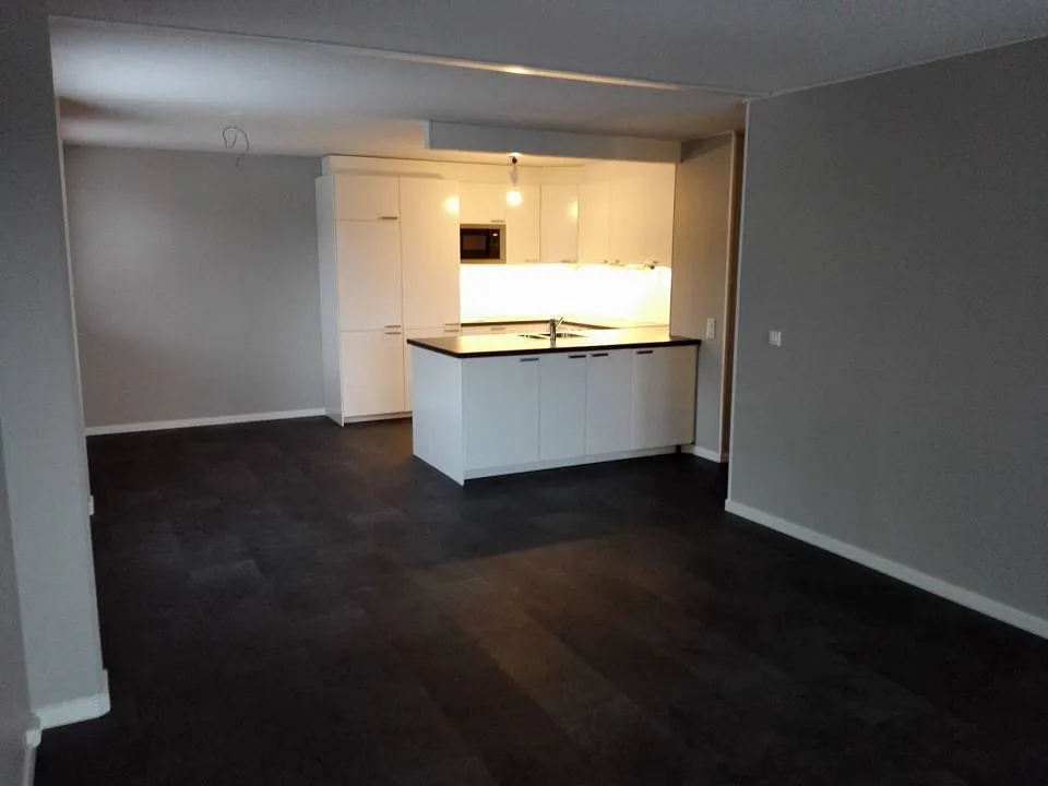 Sisätila, jossa on tumma puulattia, valkoiset keittiökaapit ja harmaat seinät.