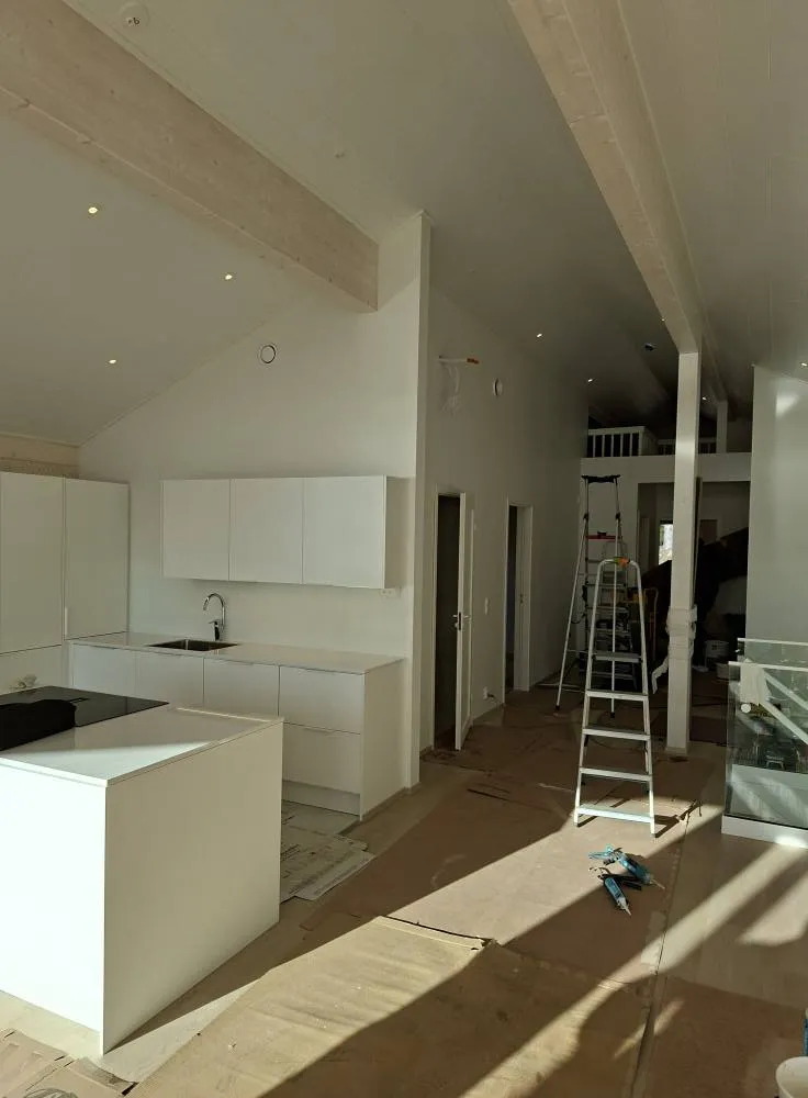 Vaalea keittiö, jossa valkoiset kaapit, saareke ja tikkaat. Auringonvalo lankeaa lattialle.