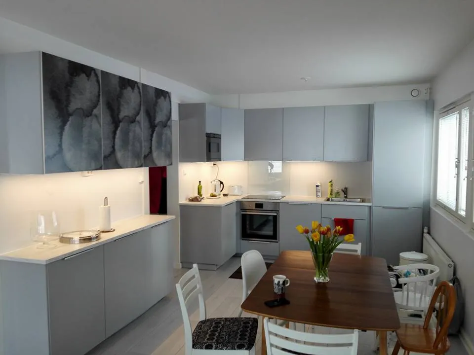 Valoisassa keittiössä on harmaat kaapit, puinen ruokapöytä tulppaaneilla ja erilaisia tuoleja.