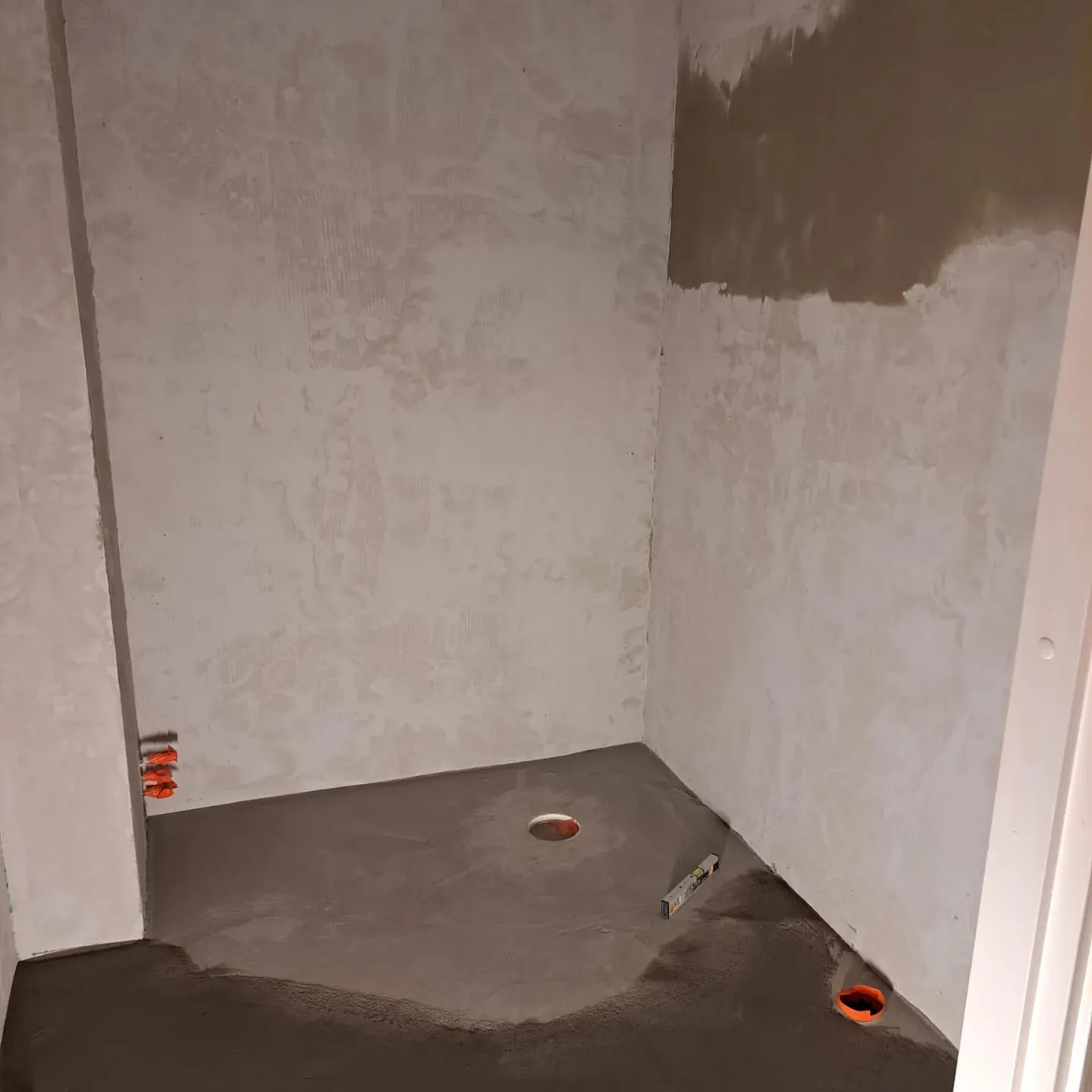 Keskeneräinen kylpyhuone, jossa on harmaa lattia, kipsilevyseinät ja oranssit putket.