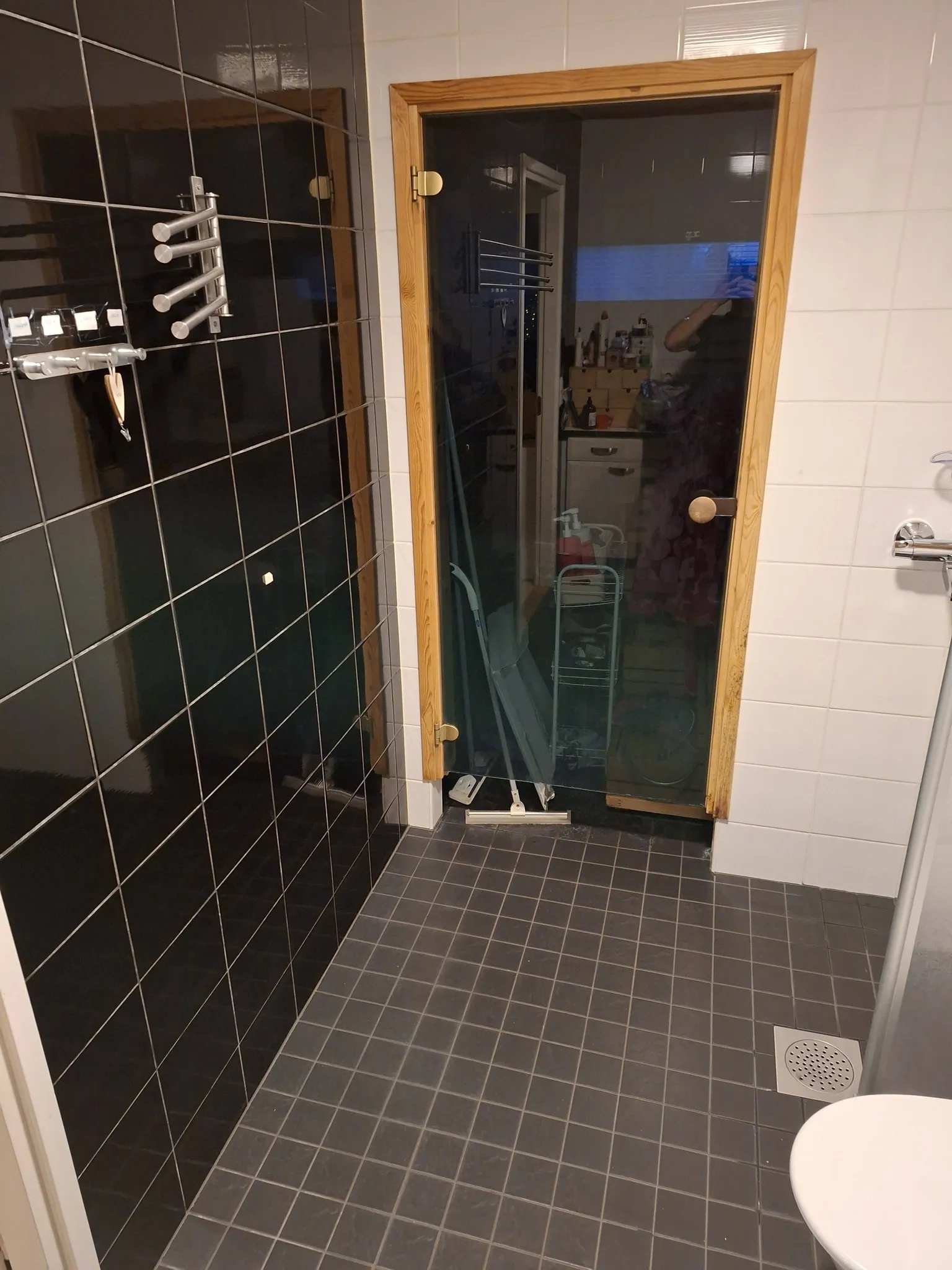 Kylpyhuoneen kuva, jossa on musta suihkukaappi, puinen lasiovi, harmaat laatat ja valkoinen pesuallas.