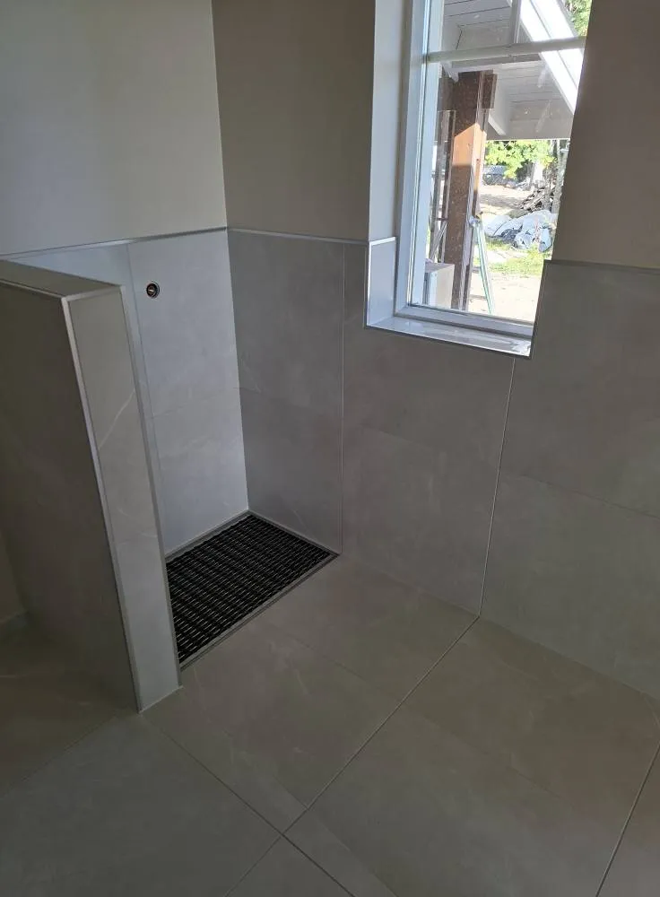 Vaaleanharmaa laatoitettu huone, jossa on ikkuna ja musta ritilä lattiassa.