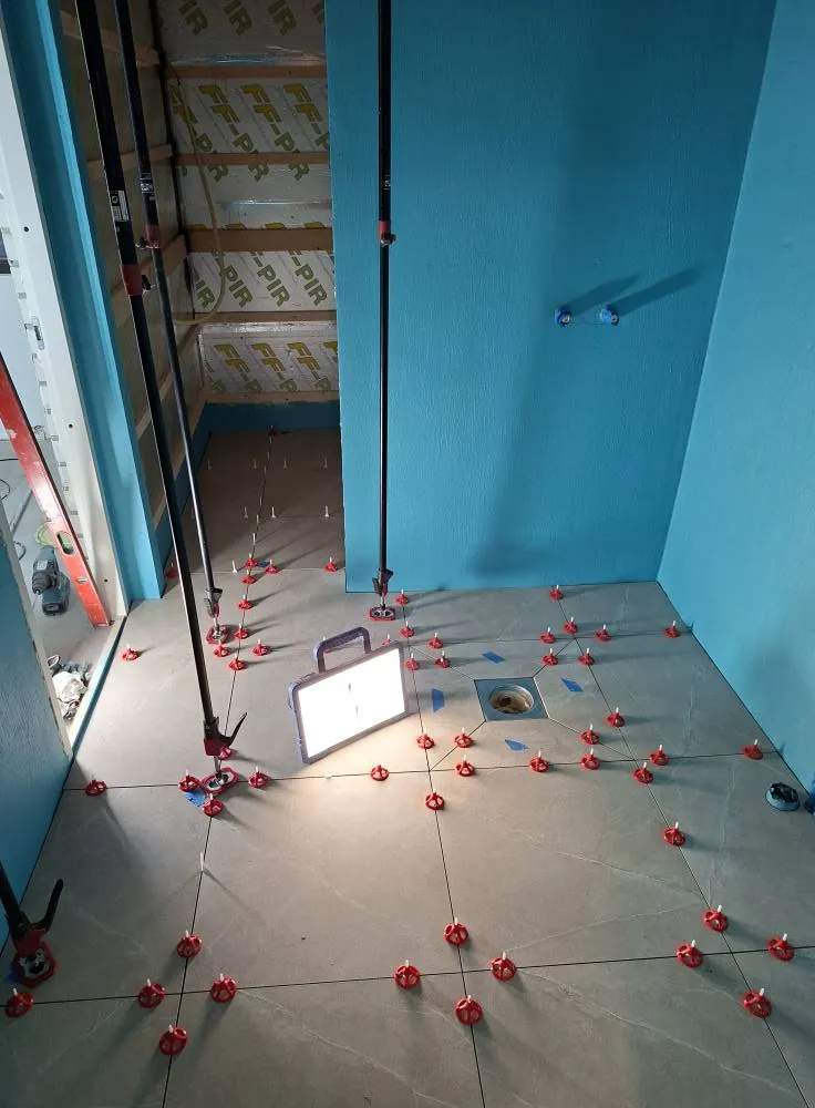 Kylpyhuoneen lattia on laatoitettu harmailla laatoilla, joissa on punaiset laatoitustuet. Seinät ovat turkoosit ja katto on eristetty. Työvalo valaisee lattiaa.