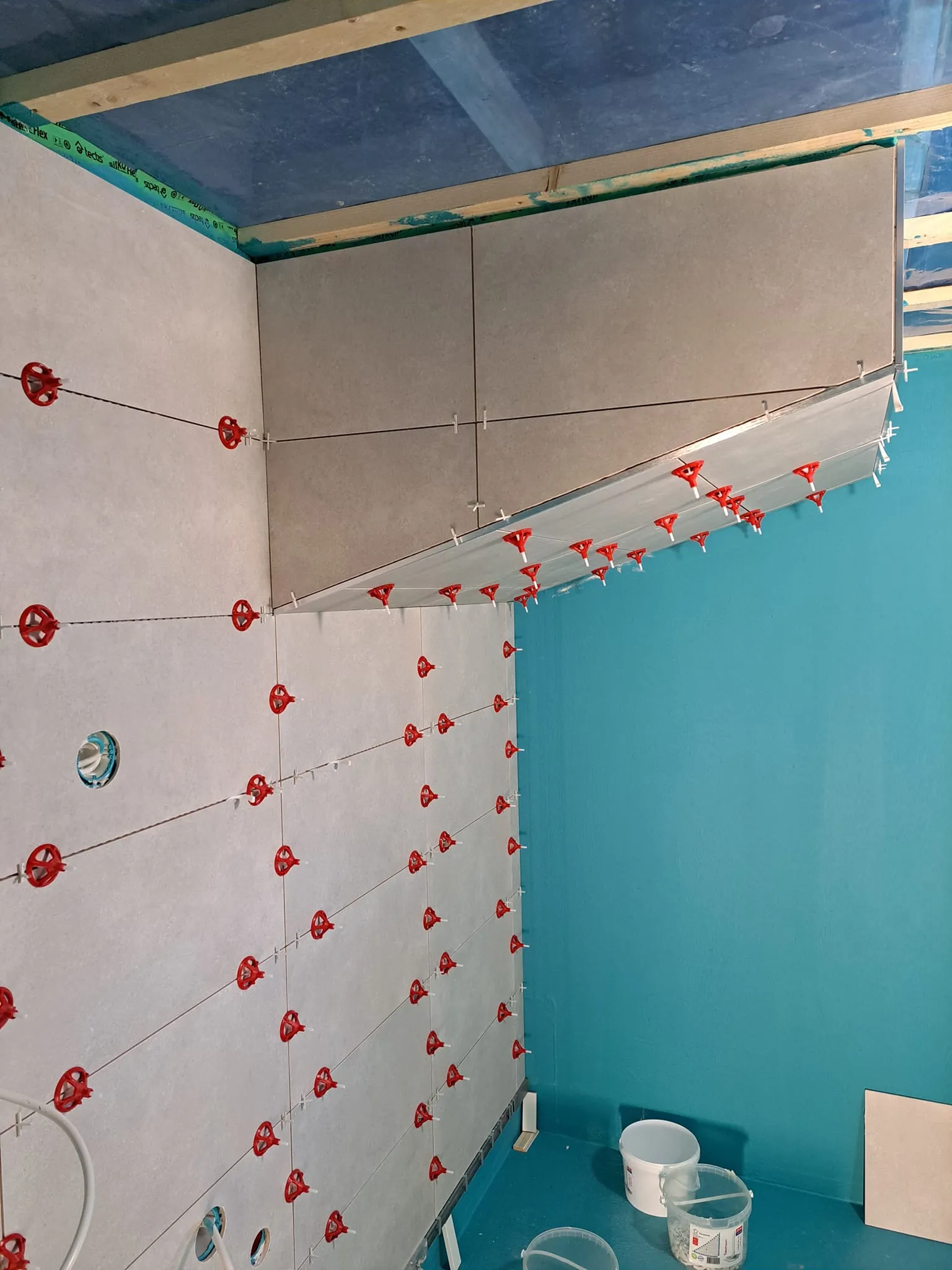 Keskeneräinen kylpyhuone, jossa on harmaat laatat, punaiset kiinnikkeet ja siniset seinät.