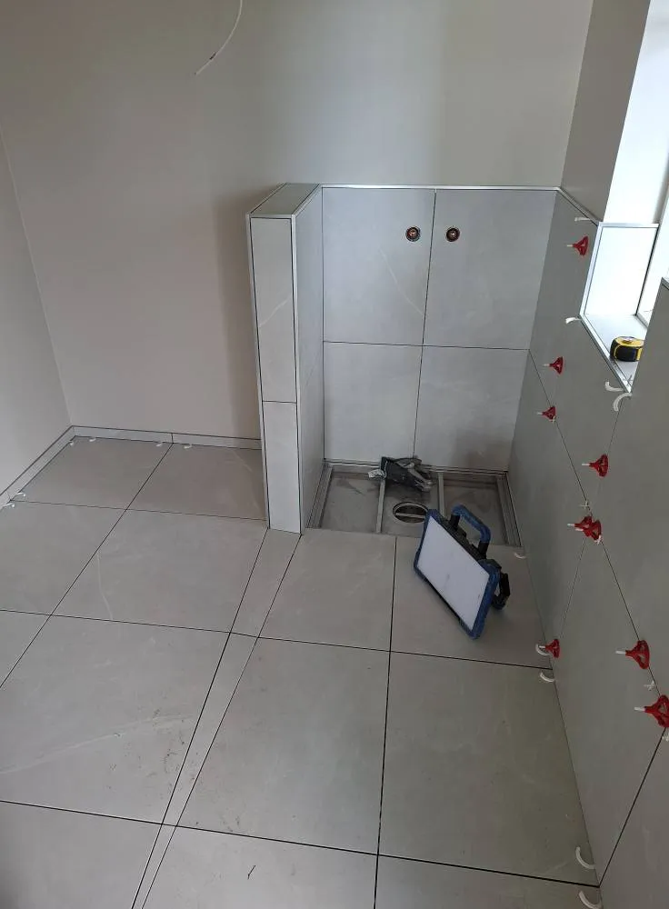 Kylpyhuoneen lattia- ja seinälaatoitus on kesken, näkyvissä on laattoja, työkaluja ja punaisia kiiloja.