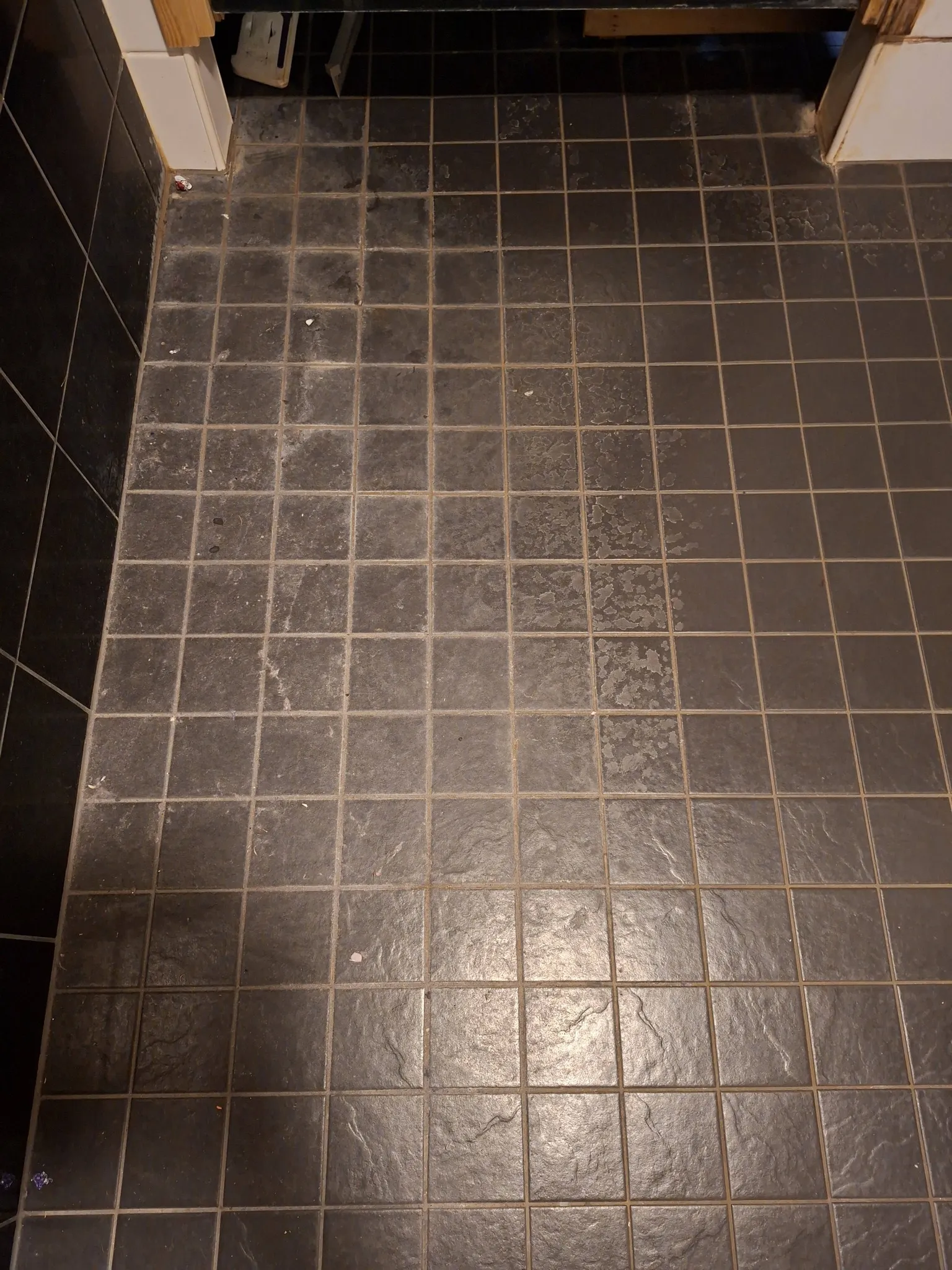 Tummanharmaat lattialaatat, osittain puhdistettu, valaistus epätasainen.