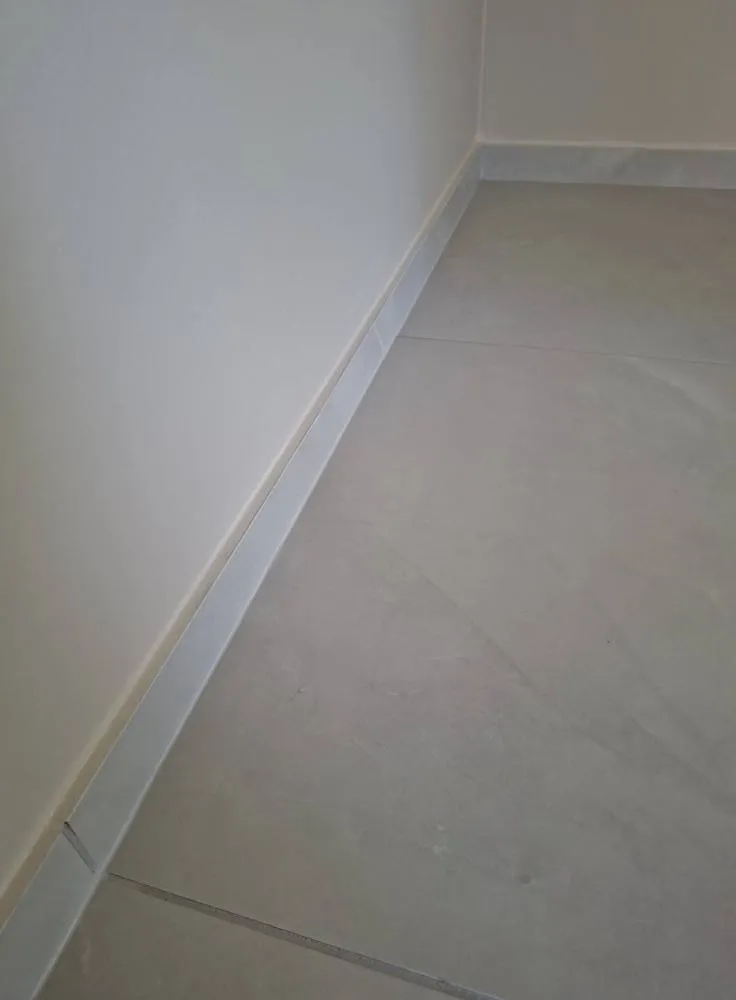 Vaaleanharmaat lattialaatat ja seinä, jossa on harmaa jalkalista. Valoisa ja moderni sisustus.