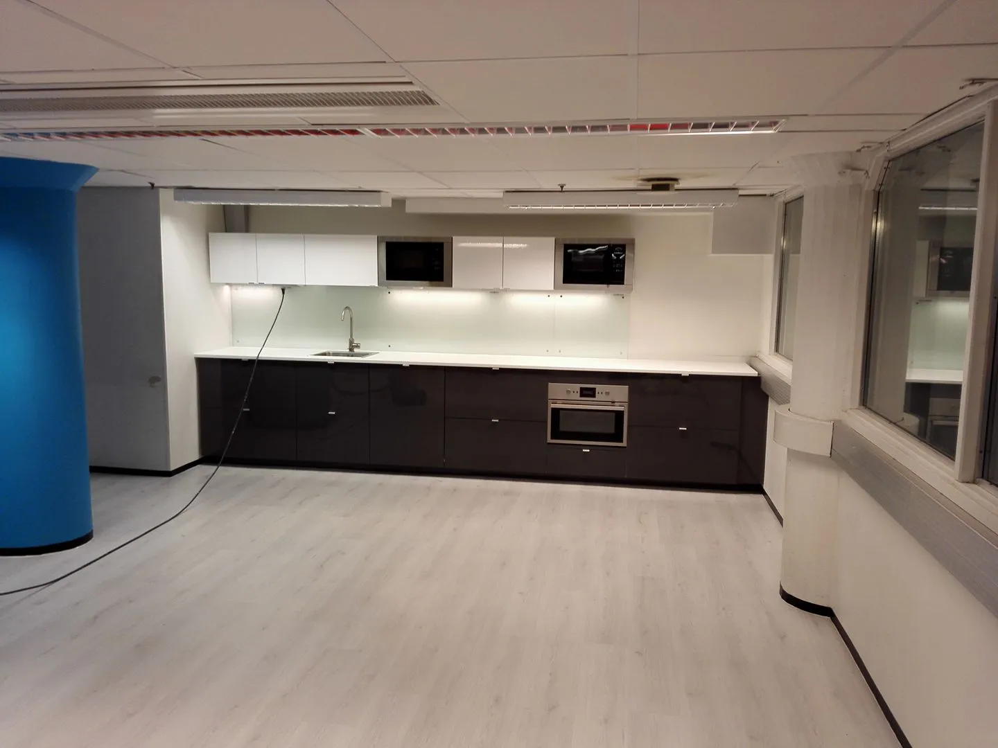 Moderni keittiö, jossa on valkoiset yläkaapit, tummat alakaapit, vaalea työtaso ja vaalea lattia.