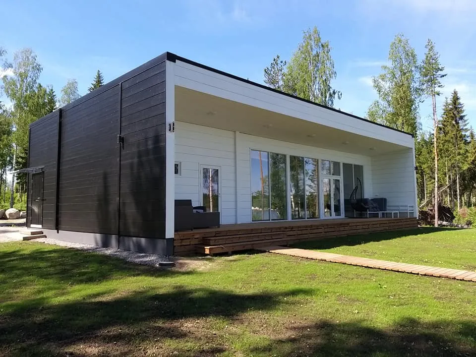 Moderni, yksikerroksinen talo, jossa on tumma puuverhous ja suuret ikkunat, valoisa sää.