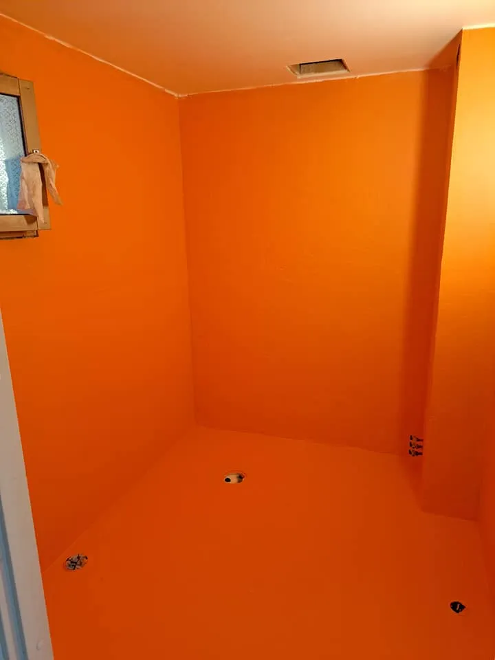 Oranssi kylpyhuone, jossa on ikkuna, ilmanvaihtoaukko katossa ja viemärit lattiassa, valaistus on kirkas.