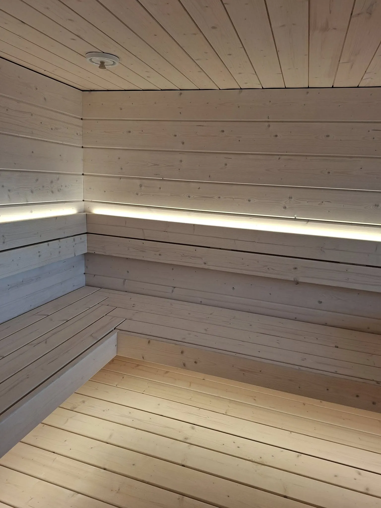 Vaalea puusauna, jossa on penkit, seinät ja katto puusta, sekä epäsuora valaistus.