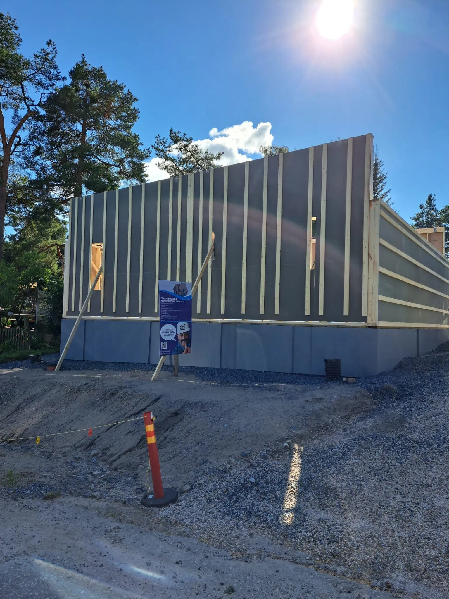 Rakenteilla oleva talo, jossa harmaa pohja ja puurunkoinen seinä, aurinkoinen sää.