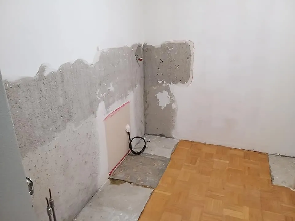 Huone remontin alla, seinät osittain rapattu, lattialla parkettia ja betonia, valoisa.