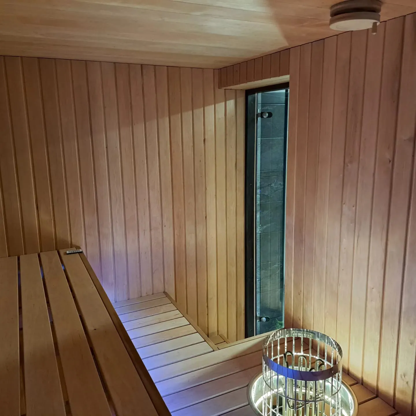 Sauna, jossa on puupanelointi, puinen penkki, lasiovi ja metallinen kiuas.