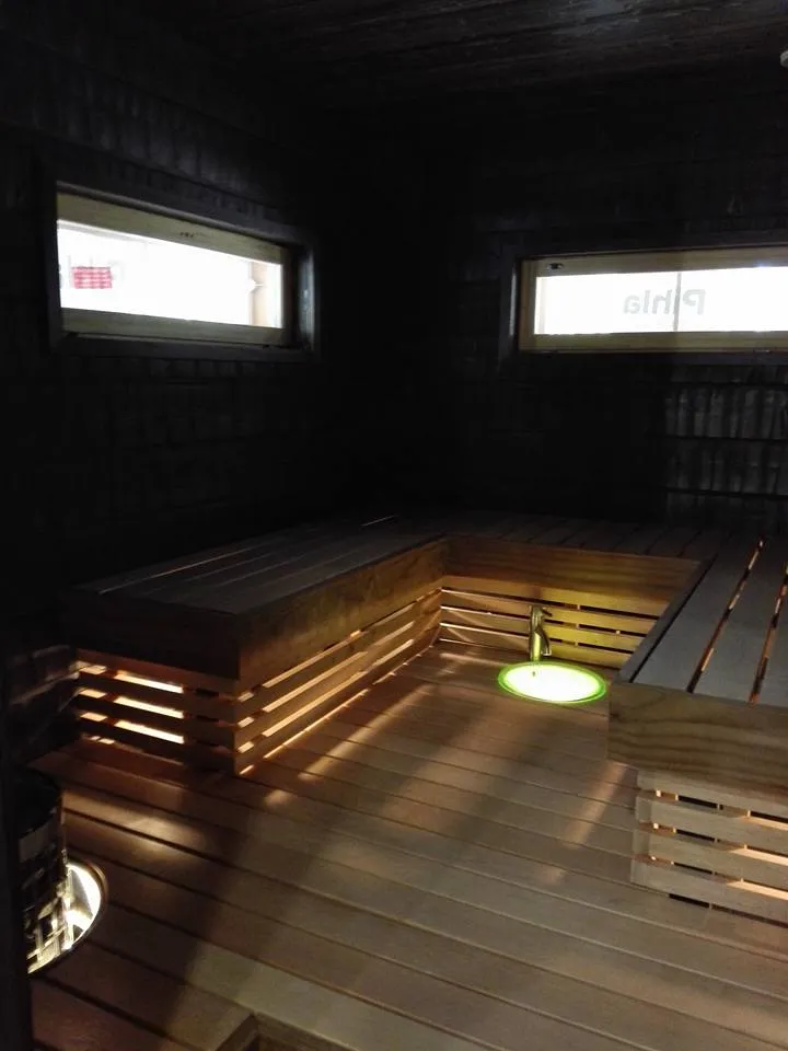 Sauna, jossa on puupenkit, kaksi ikkunaa ja vihreä valo lattialla.