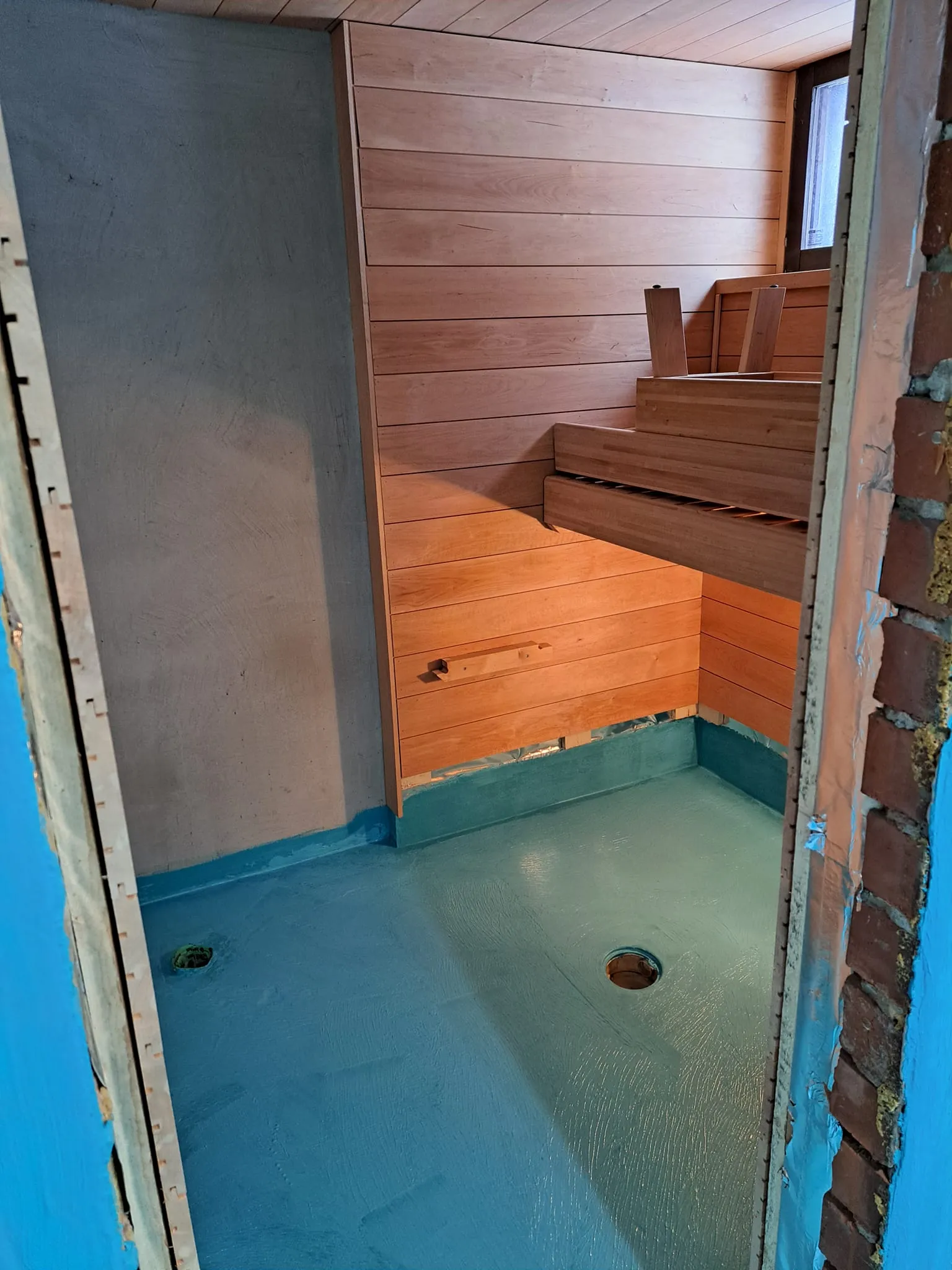 Valokuva rakenteilla olevasta saunasta, jossa on puupanelointi, sininen lattia ja ikkuna.