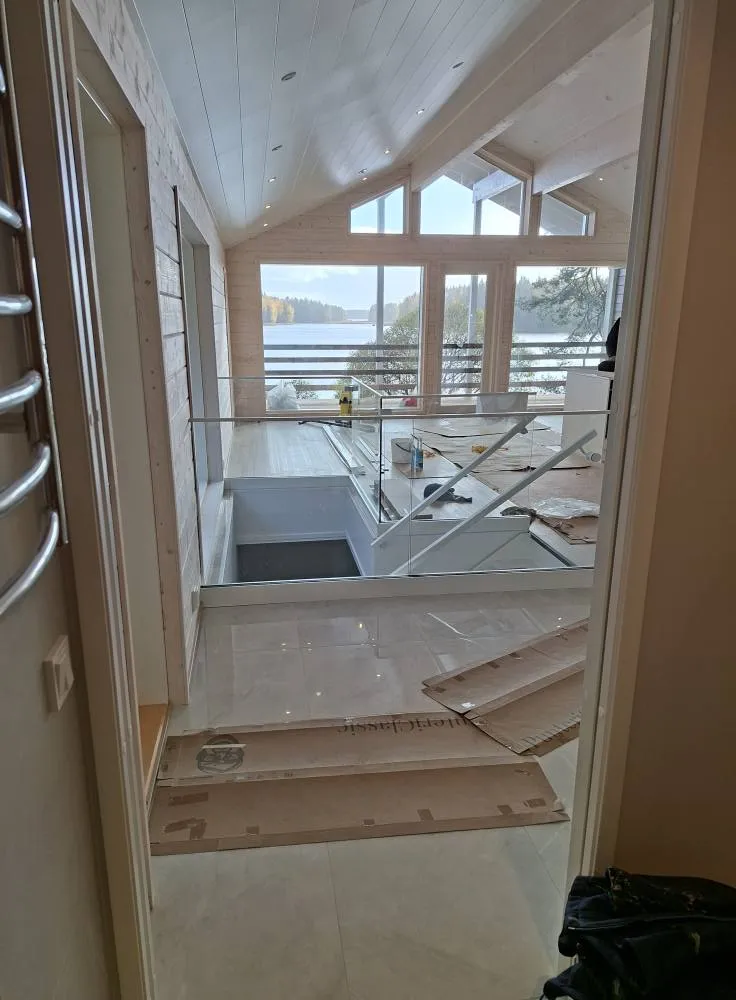 Sisätiloissa näkyy lasikaiteella varustettu portaikko, valoisa huoneisto ja järvimaisema ikkunoiden takana.