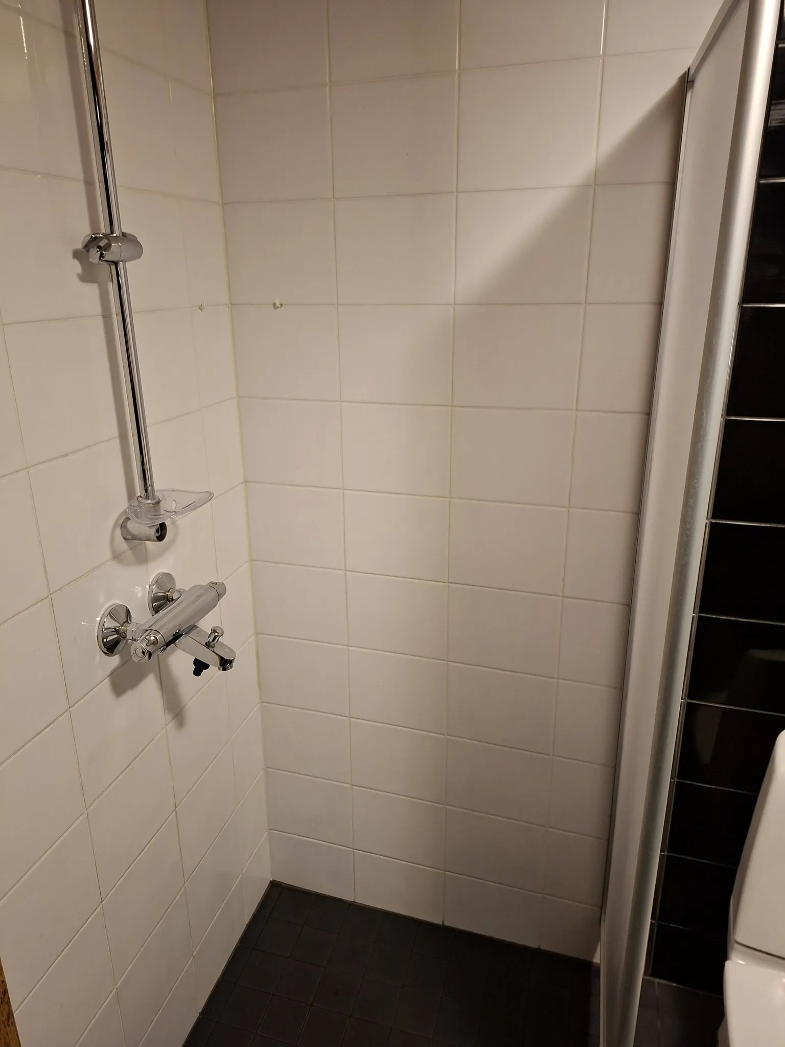 Valkoinen suihku, jossa on krominen suihkuputki ja musta lattia.