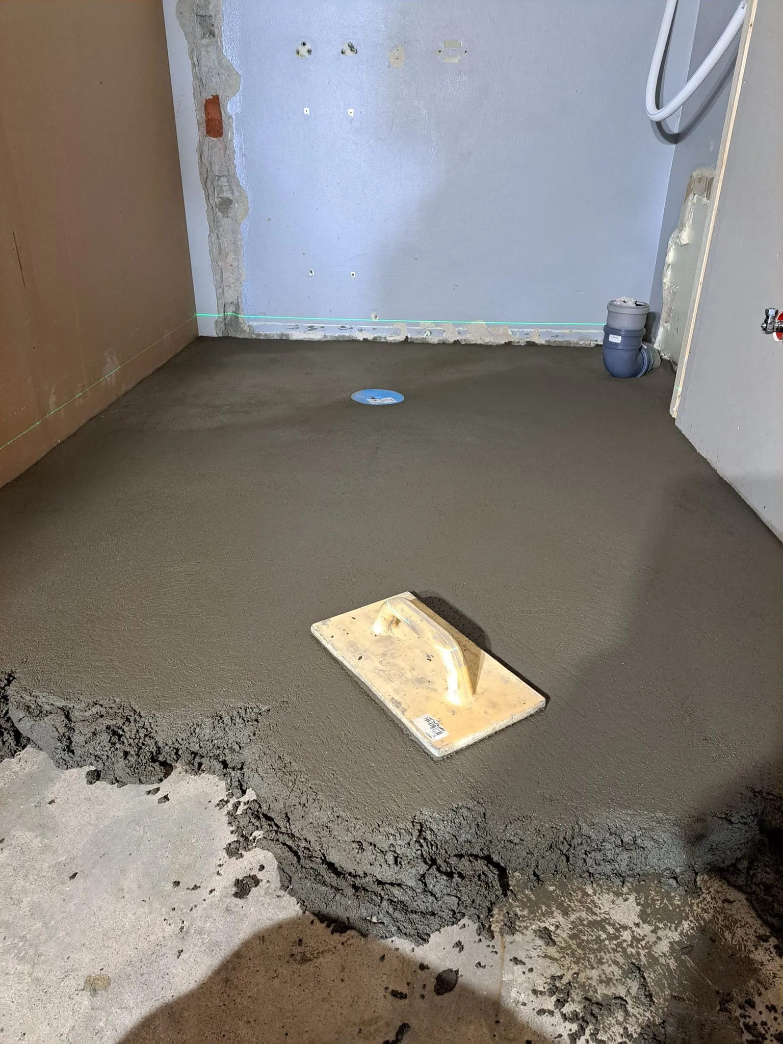 Huoneessa on tasoitettu lattia, jossa on kelluva laasti ja kelluke. Seinät ovat harmaat ja valaistus on kirkas.