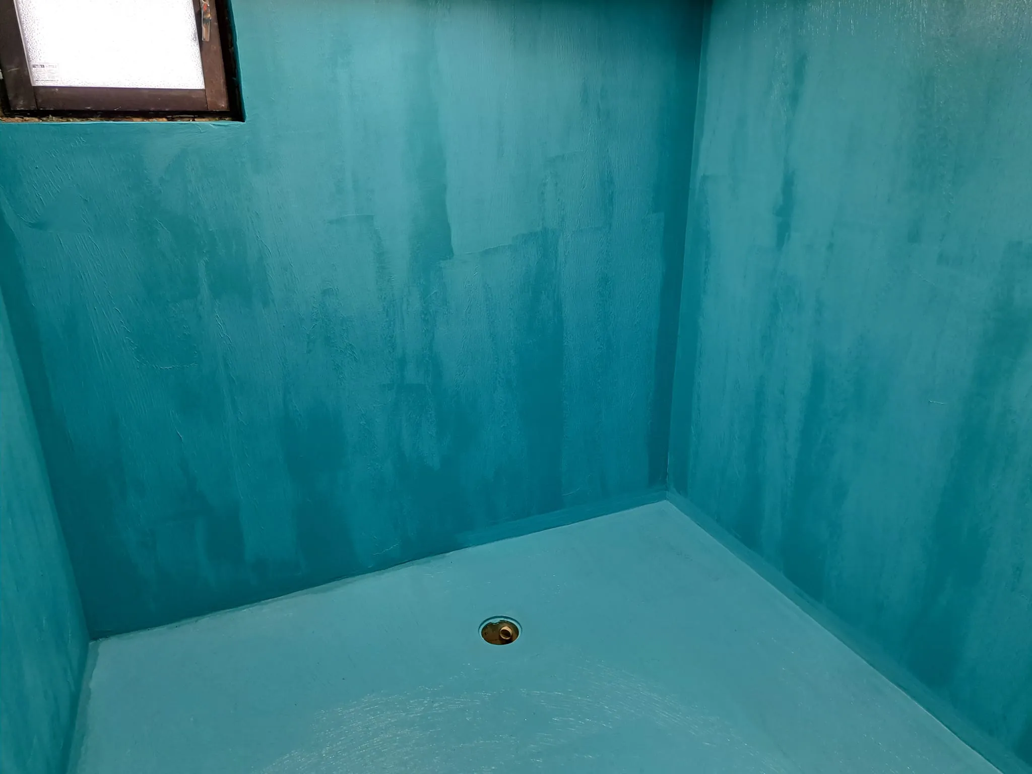 Turkoosi, maalattu suihkutila, jossa on ikkuna ja viemäri.