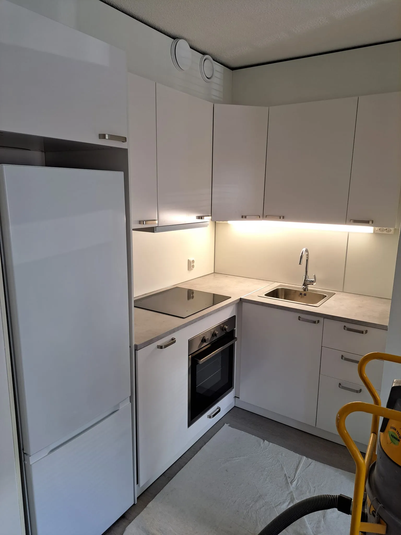 Valkoinen keittiö, jääkaappi, liesi ja siivousvälineet.